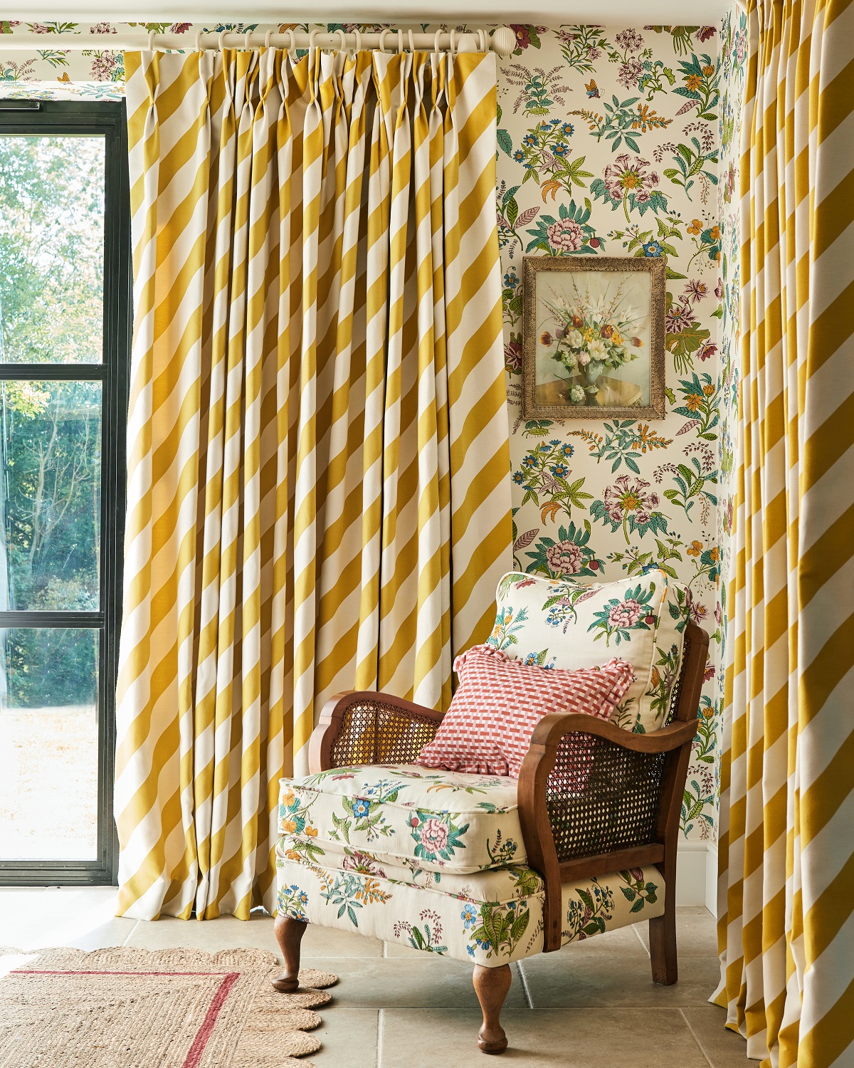 a corner of a room with bold yellow striped full length curtains behind a contrasting chair upholstered in floral fabric