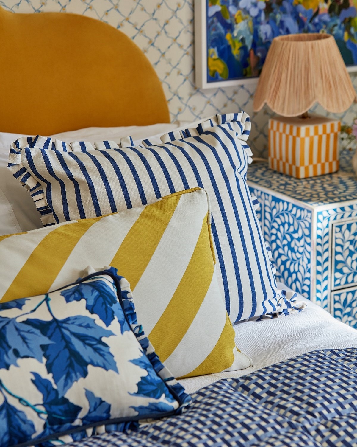 detail of a bed with yellow upholstered headboard and an eclectic mix of fabric cushions in yellow and blue stripes and patterns from Harlequin