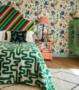 Botanical wallpaper, bright striped headboard and bold green patterned throw above the bed