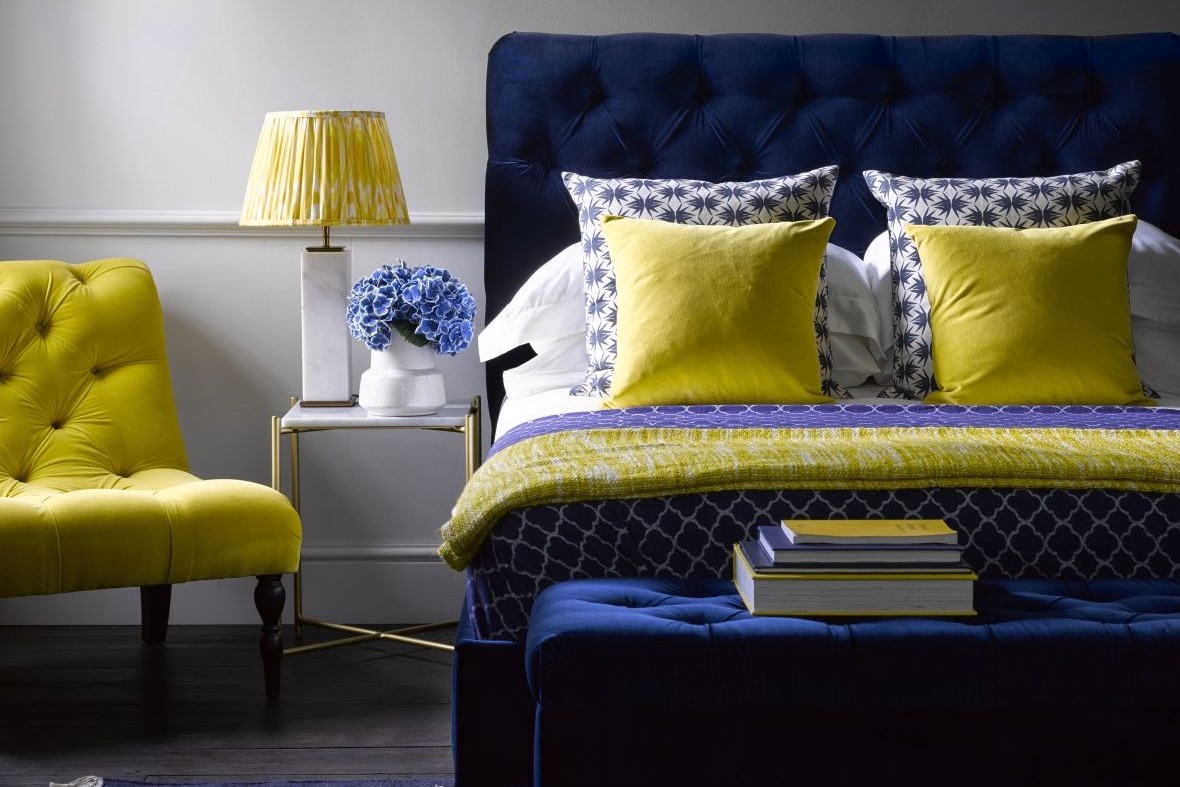 prussian blue upholstered headboard with blue and white patterned cushions and bright yellow accessories