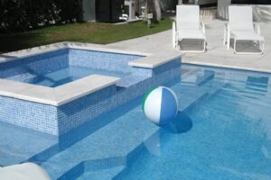swimming pool with blue mosaic tiles, a white surround and a floating blue and white beachball