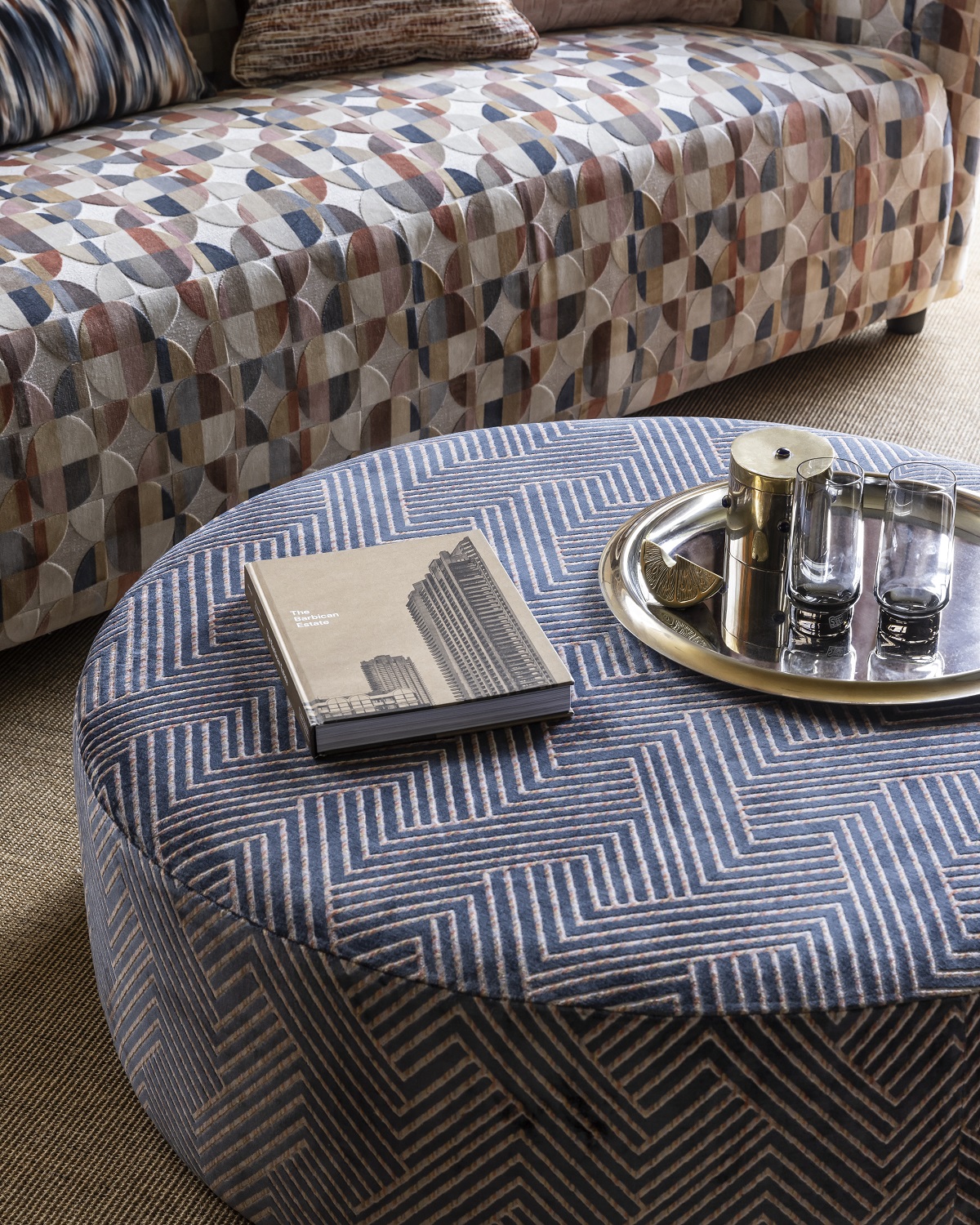 detail of fabric on an upholstered table ottoman next to a patterned couch covered in Urban fabric collection