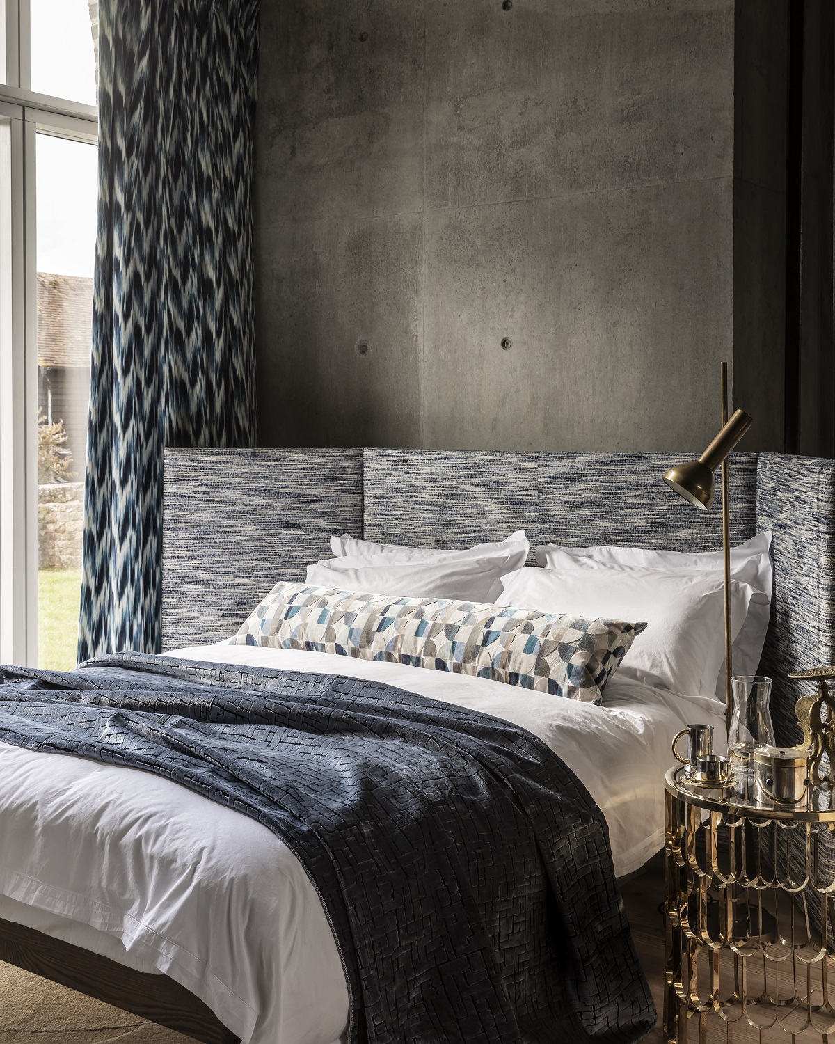 screen shaped headboard against a grey concrete wall with a mix of patterns and fabric on the bed
