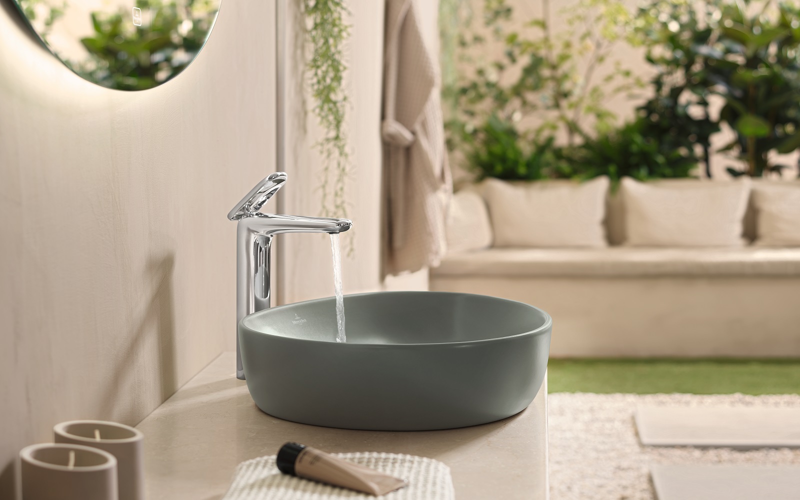moss green rounded washbasin by villeroy & boch with water from tap and greenery in the background