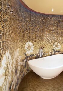 curved bathroom wall in gold floral mosaic running behind white freestanding bath