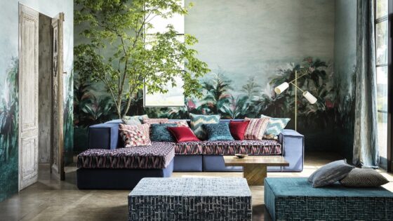 patterned upholstered couch with a pile of contrasting cushions in a room with plants and natural light
