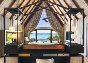 view from behind the bed across the guestroom with pitched beam ceiling out to the ocean in the maldives