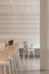 corner of restaurant in minimalistic pale timber with cut out shapes in the ceiling and in the chairs