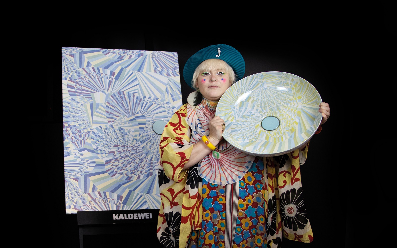 designer Bethan Laura Wood in colourful kimono and beret holding colourful basin from her collection for Kaldewei