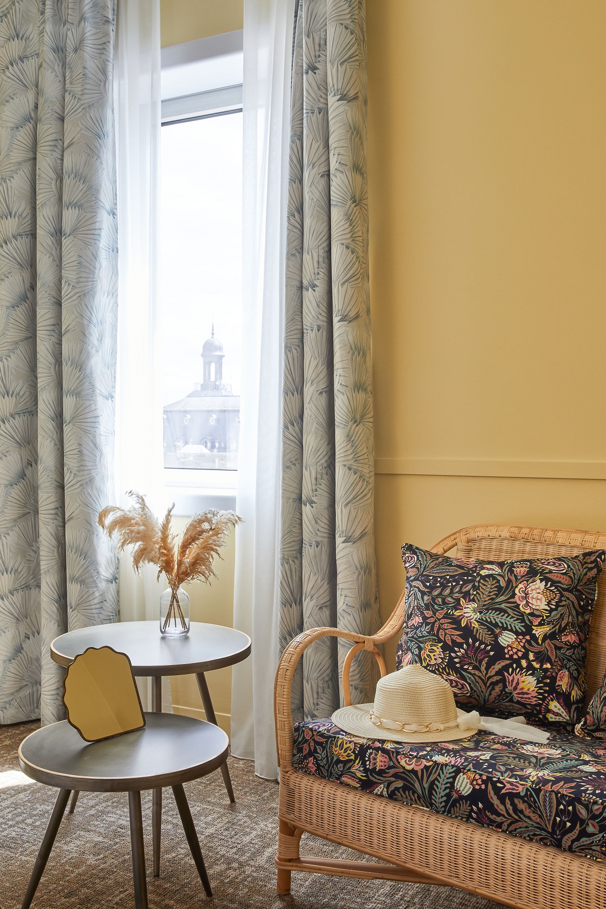 two round retro sidetables next to a wicker chair in floral upholstery with a hat on the seat