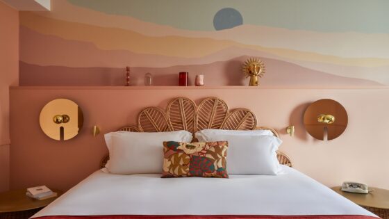 sunset tones mural painted on the wall behind a bed with a wicker headboard and brass sidelamps in hotel Indigo bordeaux