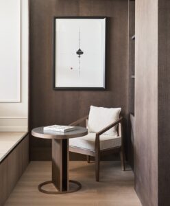 brown wood panelling and shelving in a corner with wooden chair and minimalist table with a book