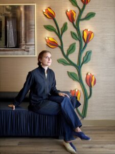 interior designer Beata Heuman sitting on a couch in front of floral light installation in Hôtel de la Boétie