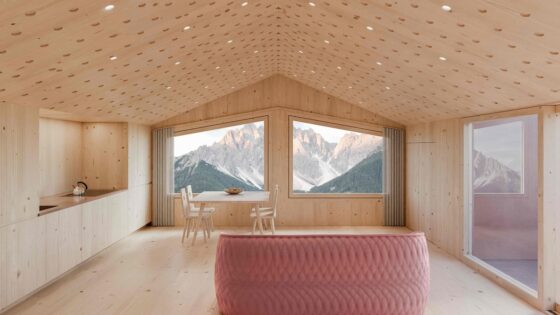 dusty pink couch and wooden table and chairs in stark minimalist interior with mountain view