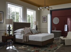 bedroom with bed set against windows with patterend cushions on the bed and bedside table and large lamp