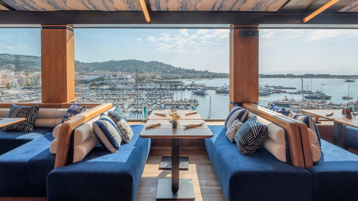 blue bench seating on either side of tables set for breakfast with views over Cannes and the Mediterranean