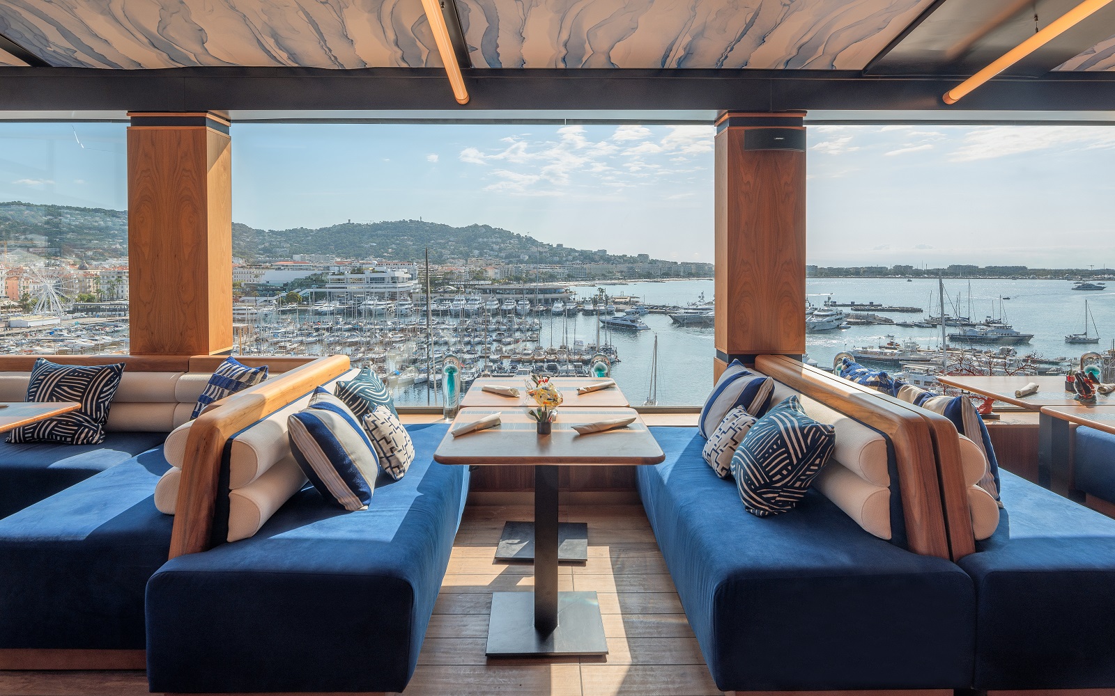 blue bench seating on either side of tables set for breakfast with views over Cannes and the Mediterranean