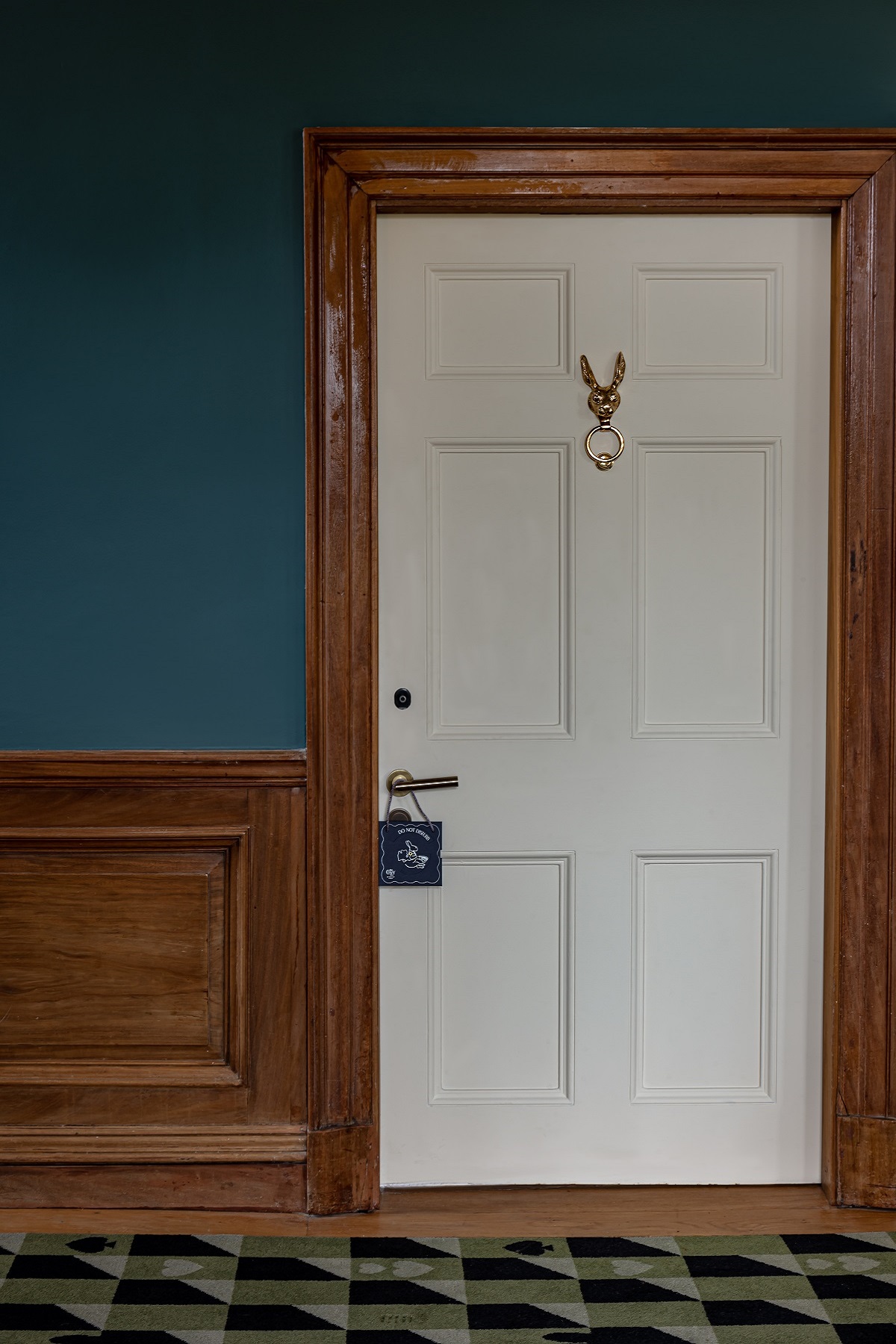 white guestroom door with a rabbit knocker and wood surround set in a blue wall