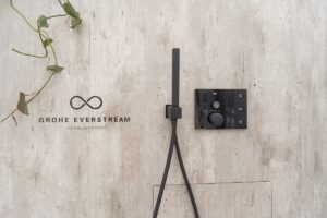 The GROHE Everstream shower in black fitted onto a stone wall with a plant in the background