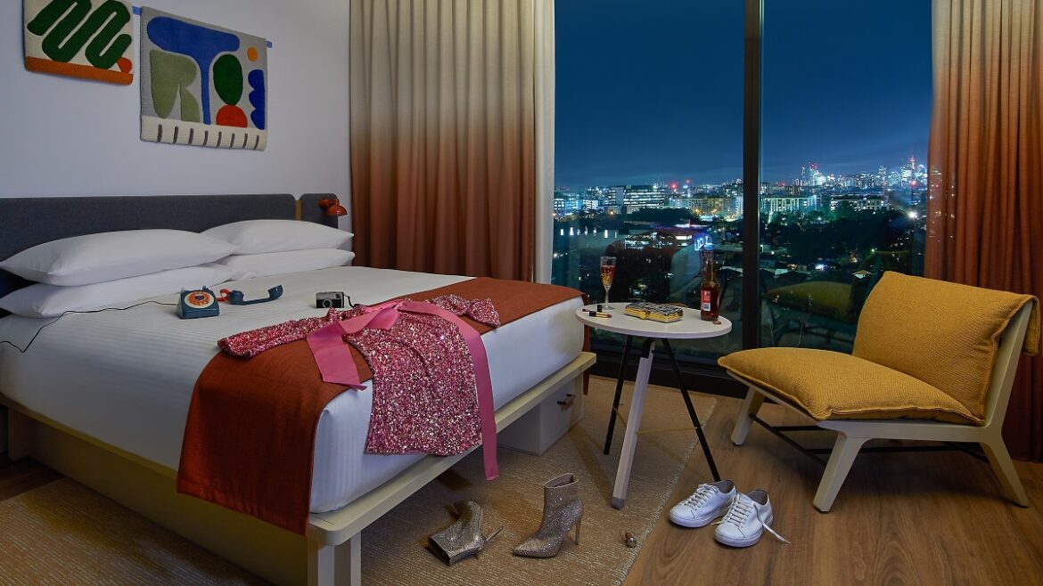 guestroom with window looking out over the city at night and vintage phone on the bed next to items of clothing