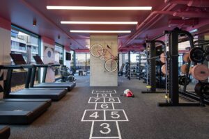 gym equipment alongside hopscotch squares painted on the floor and a moxy bicycle hanging on the wall
