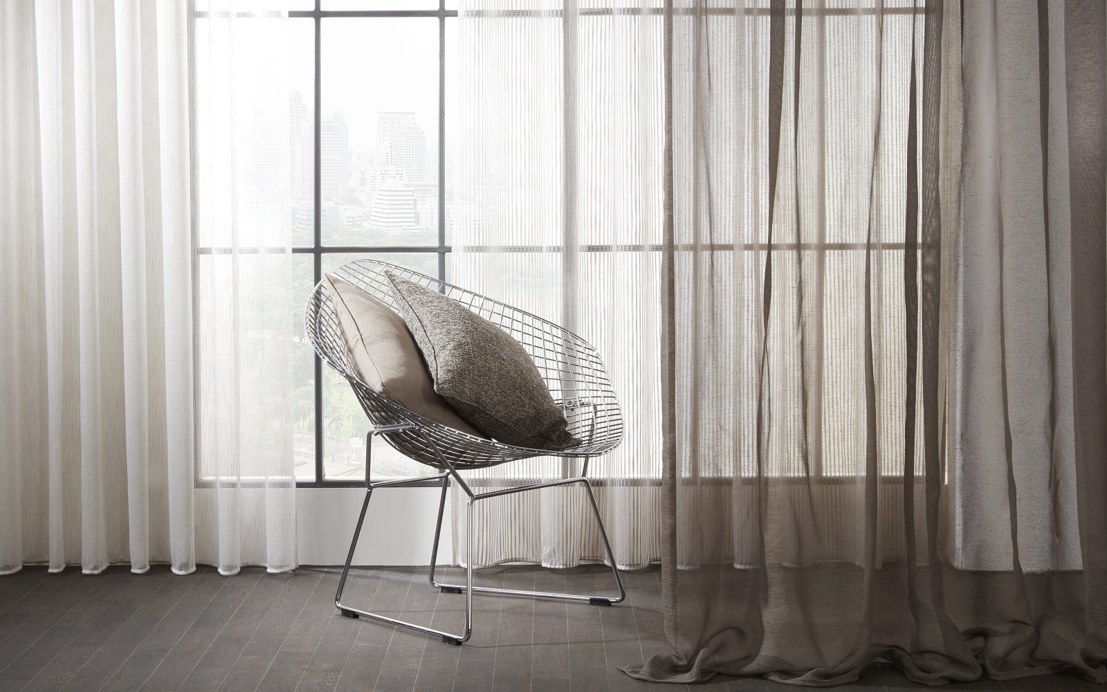 wire frame chair in front of a window with floor to ceiling voile curtains in mixed tones of grey