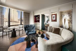 curved cream couch on patterned carpet with view out to the city in the Raffles Boston guestroom designed by Stonehill Taylor