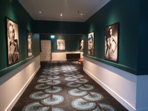 casino and hotel corridor with blue patterned carpet and lighting focussed on black and white portraits on the blue wall