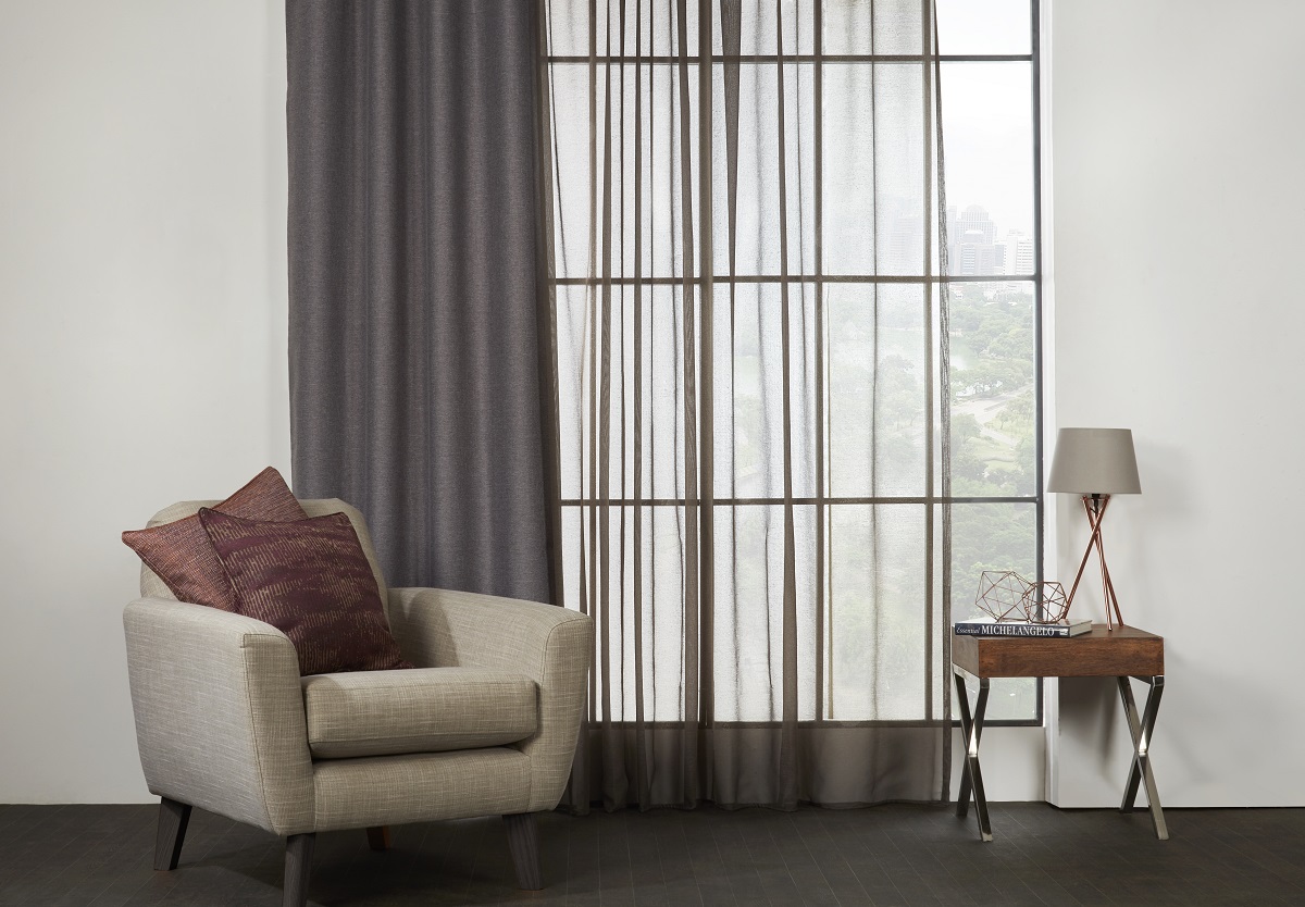 grey voile next to solid grey curtain in floor to ceiling window with cream chair in front