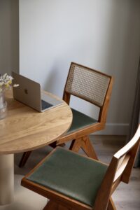 detail of seating in Bob W apartment with wooden table, mid centrury modern wooden chairs and a laptop open on the table