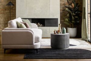 side view of cream sofa with curved edges in front of round table and fireplace