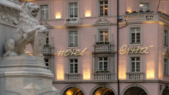the pink and grey turn of the century style facade of Hotel Citta with marble statue in foreground