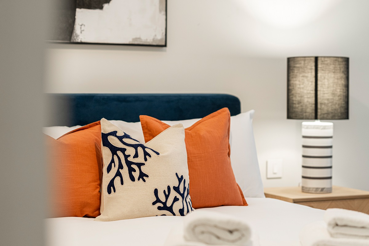 detail of soft furnishings in orange and patterned fabric on bed with white linen