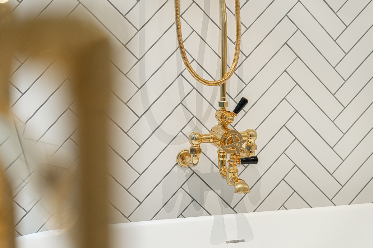 white tiled herringbone bathroom wall with gold fittings