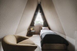 view across A frame guestroom with bed and chair all in soft tones and natural colours in hotel seeblick by NOA