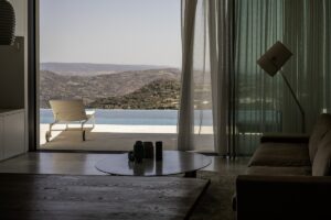 view from inside guestroom out of glass doors to terrace, swimming pool and mountain landscape in Crete