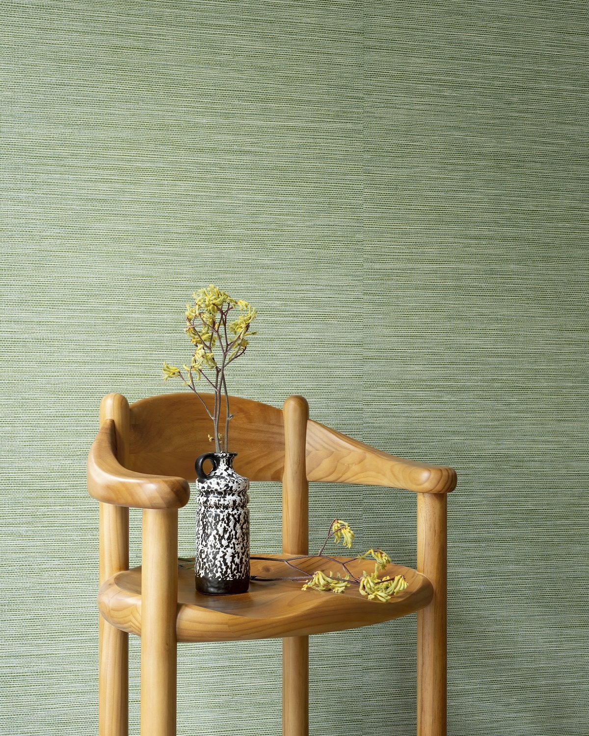 olive green textured wallcovering behind single wooden chair with vase and flowers