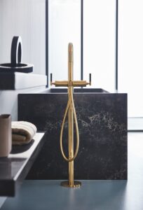 freestanding bath mixer in gold next to a black bath