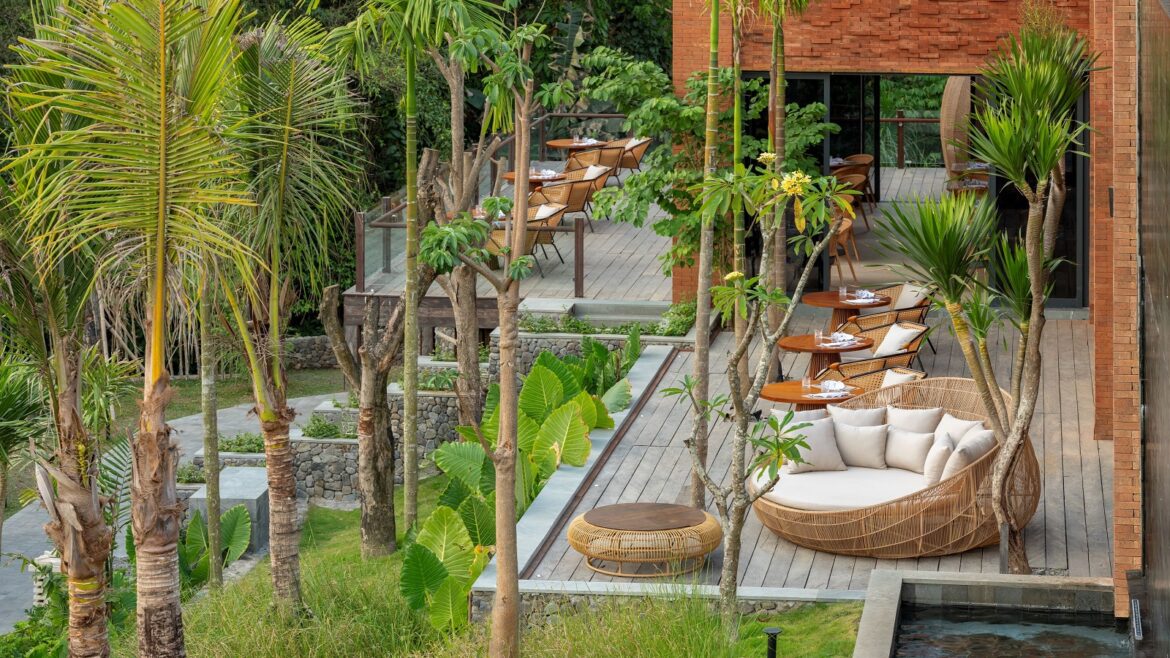 palm trees surround wooden deck with wicker lounging chairs at Garrya Bianti Yogyakarta