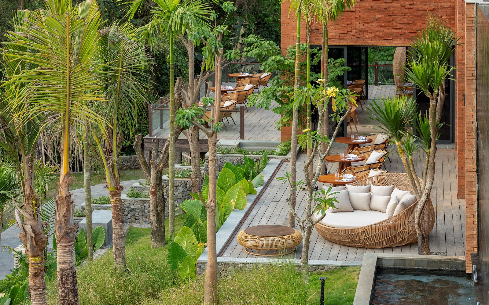 palm trees surround wooden deck with wicker lounging chairs at Garrya Bianti Yogyakarta