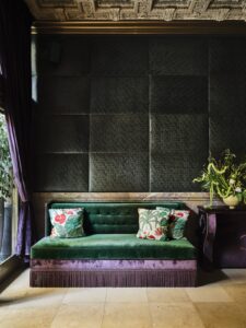 dark green and purple velvet couch against dark wall and moulded ceiling in Hotel Per La