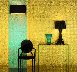 gold mosaic wall behind black chair and clear glass console table in hallway