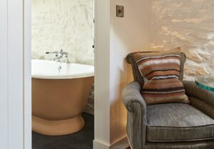 grey armchair with woven cushion next to roll top bath with a wall between