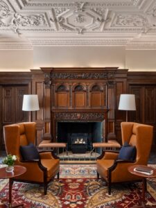 two wing back chairs in front of wooden fireplace surround in the reception of Raffles London