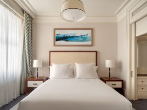 white and cream hotel suite at Raffles London with bedisde lamps in cream and wood and drum ceiling light above the bed
