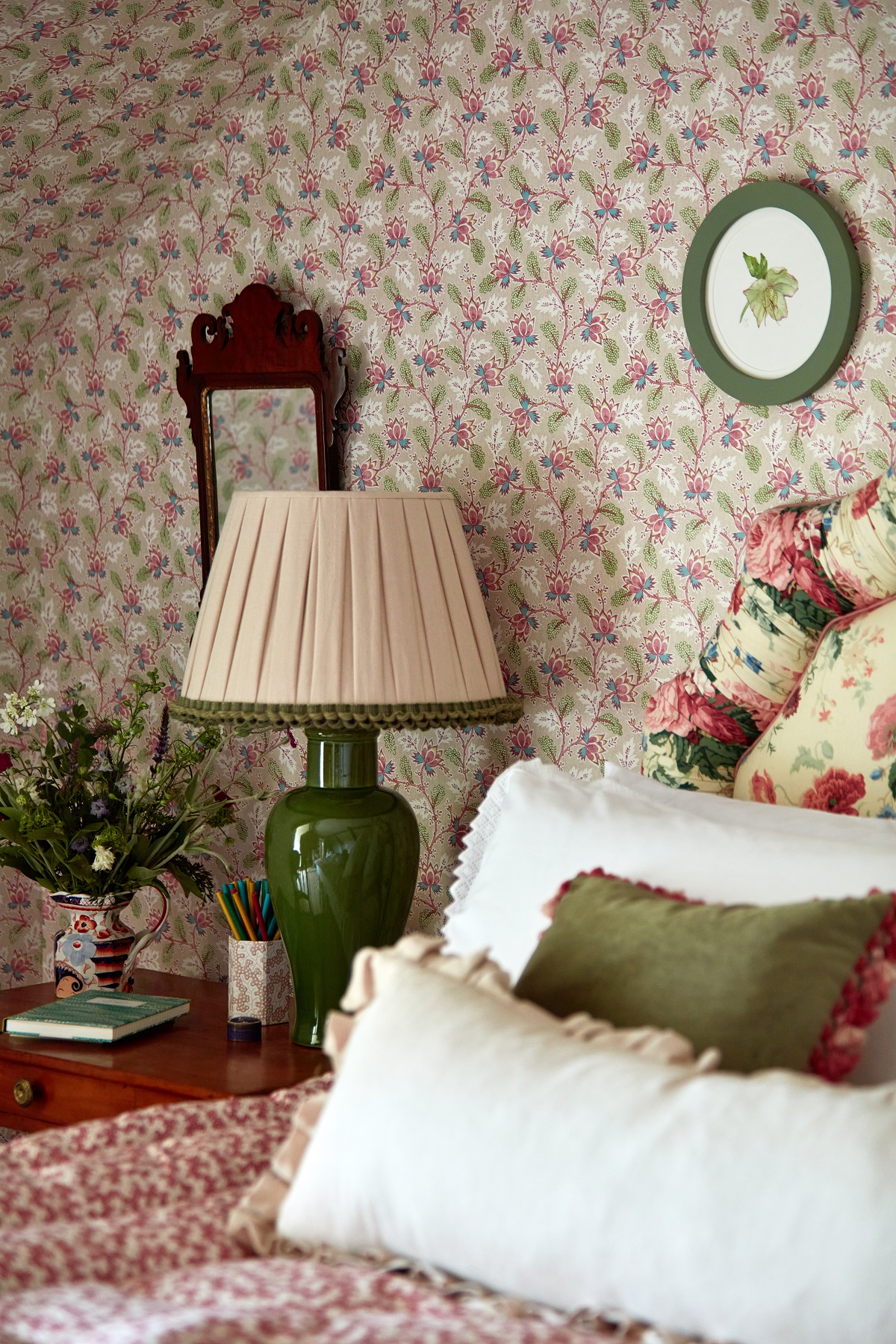 patterned wallpaper behind bed with floral patterend headboard and lamp and cushions with Sanderson trim