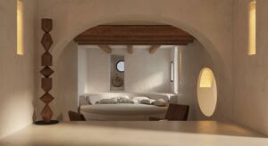 minimalist cream bedroom with bed in arched alcove with wooden ceiling and abstract wooden totem sculpture in Fincadelica Collection