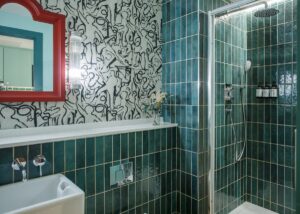bathroom with teal green tiles, a pink framed mirror and graphic black and white patterned wallpaper