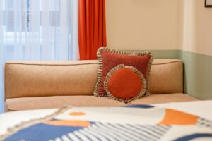 bedroom detail in room2 Belfast with bespoke throw on bed and soft furnishings in shades of orange against olive green wall