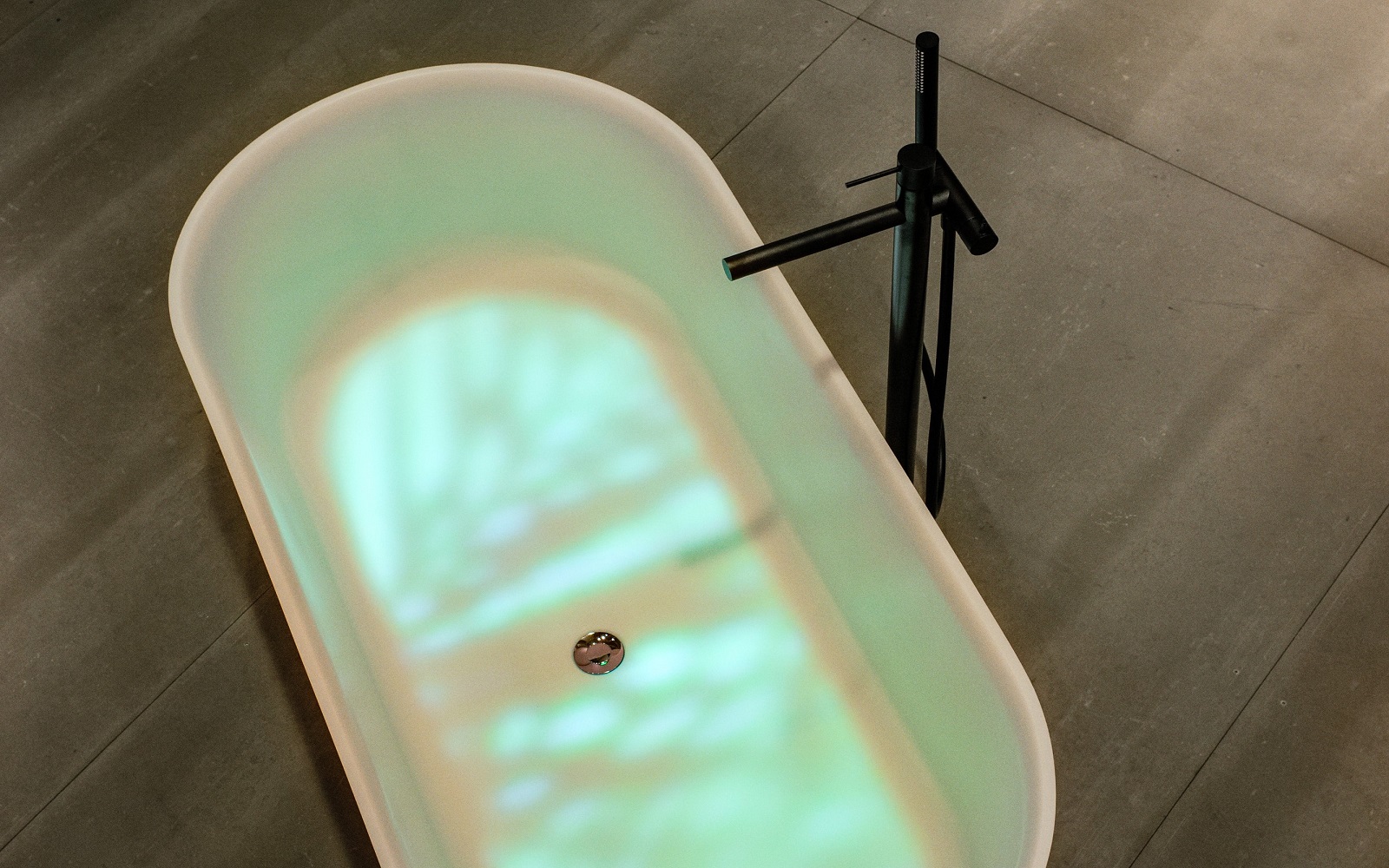 freestanding bath with light reflections in the water and black pillar tap
